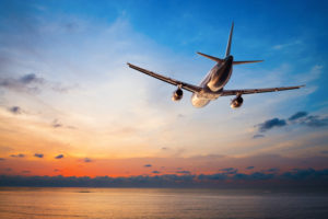 Airplane flying above tropical sea at sunse